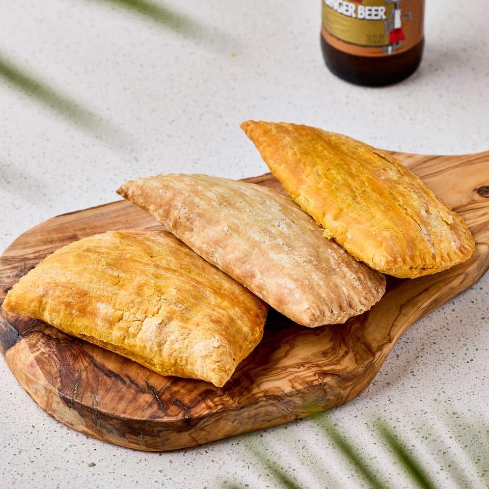 Golden and plain pastries arranged on a wooden serving board beside a bottle of Dominican Presidente beer.