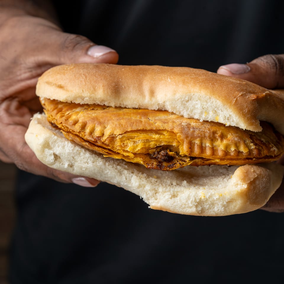 Hands hold a toasted sandwich filled with layered, golden-brown flaky pastry against a dark background.