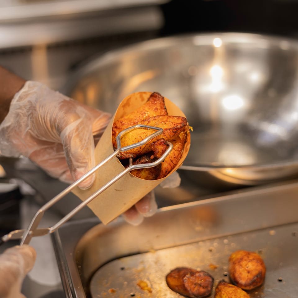 Gloved restaurant worker uses tongs to serve grilled golden-brown chicken from a hot food tray.