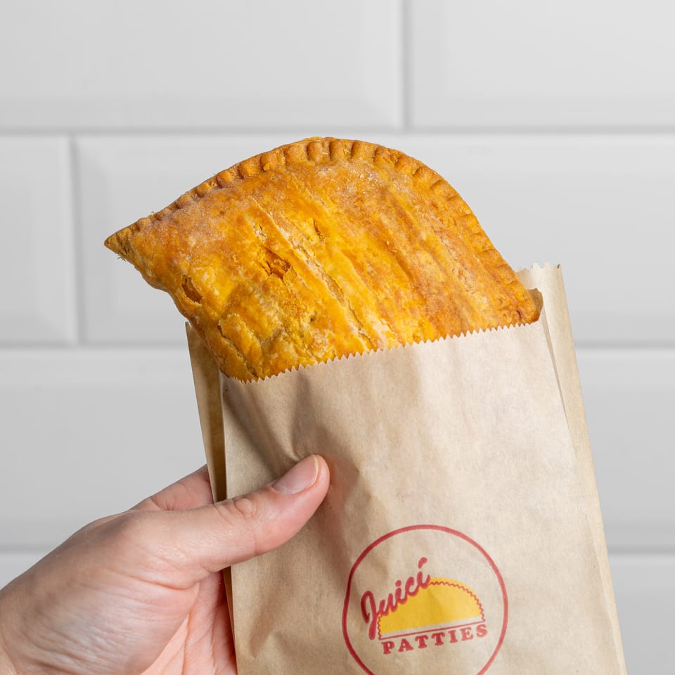 Golden-brown hand pie with a crimped crust held in a branded paper bag against a white tiled wall.