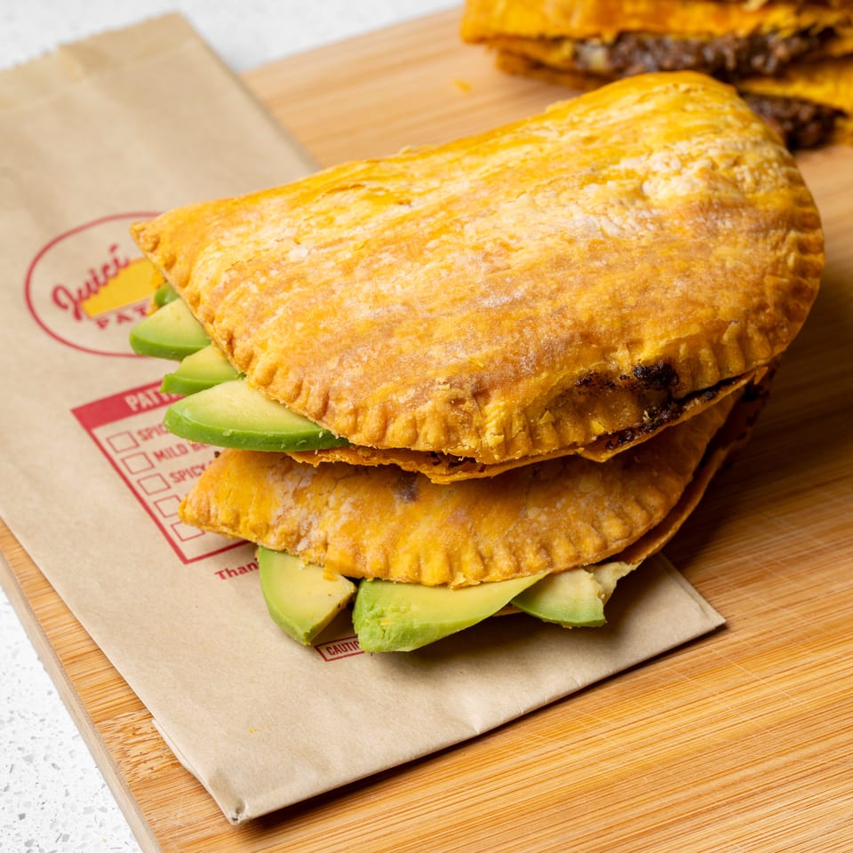 Golden fried empanada stuffed with avocado sits on branded paper beside cheeseburgers and a bottled drink.