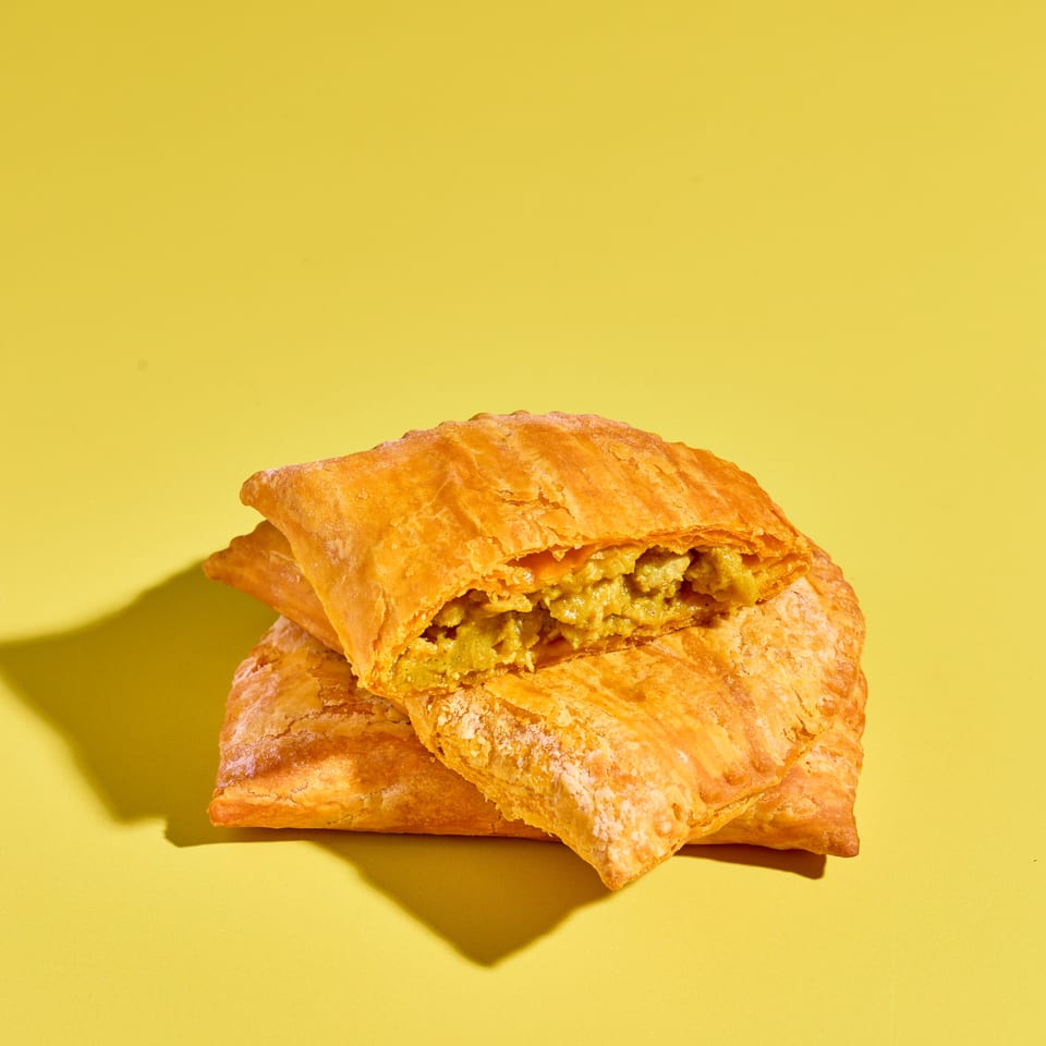 Stacked flaky golden pastries filled with savory curried chicken on a bright yellow background.