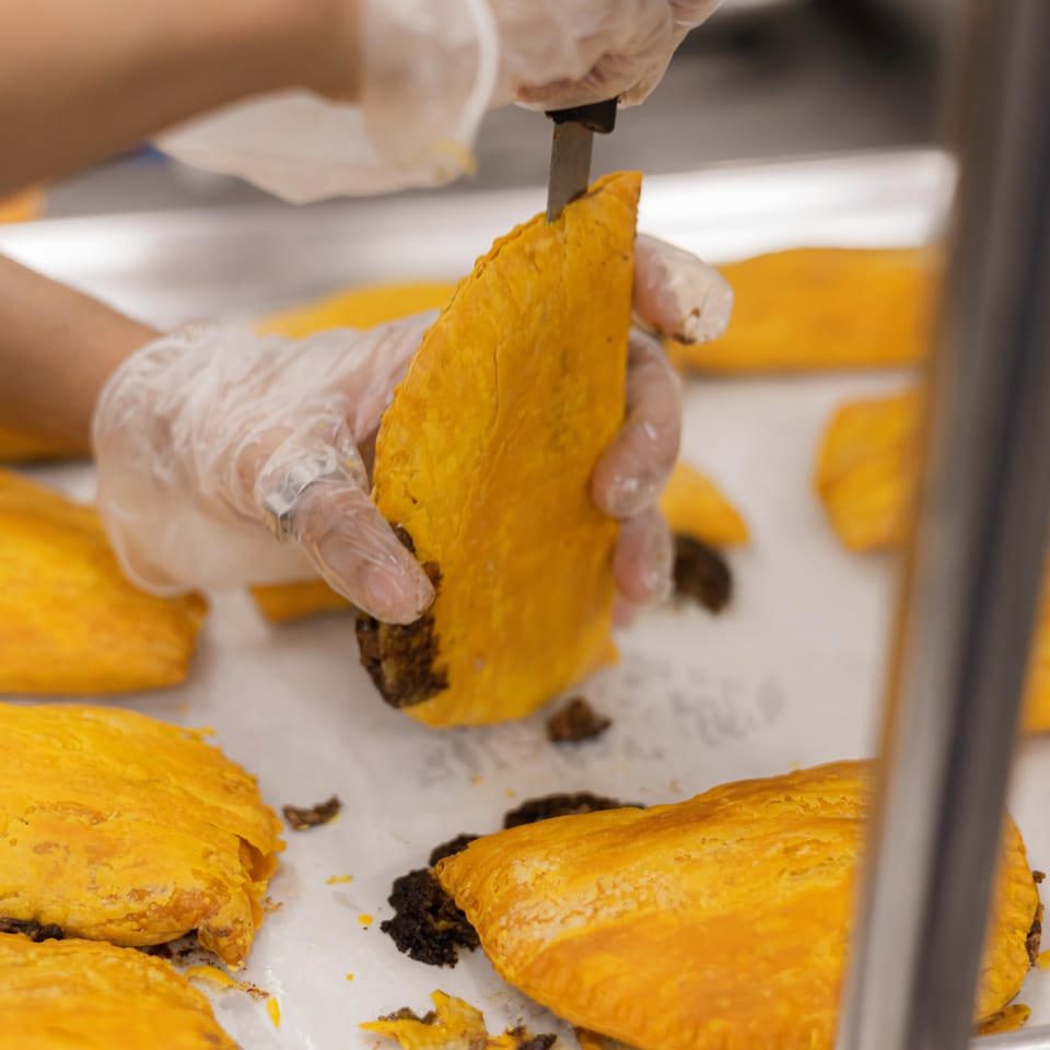 Gloved baker cuts golden laminated pastries filled with dark chocolate on a parchment-lined baking tray.
