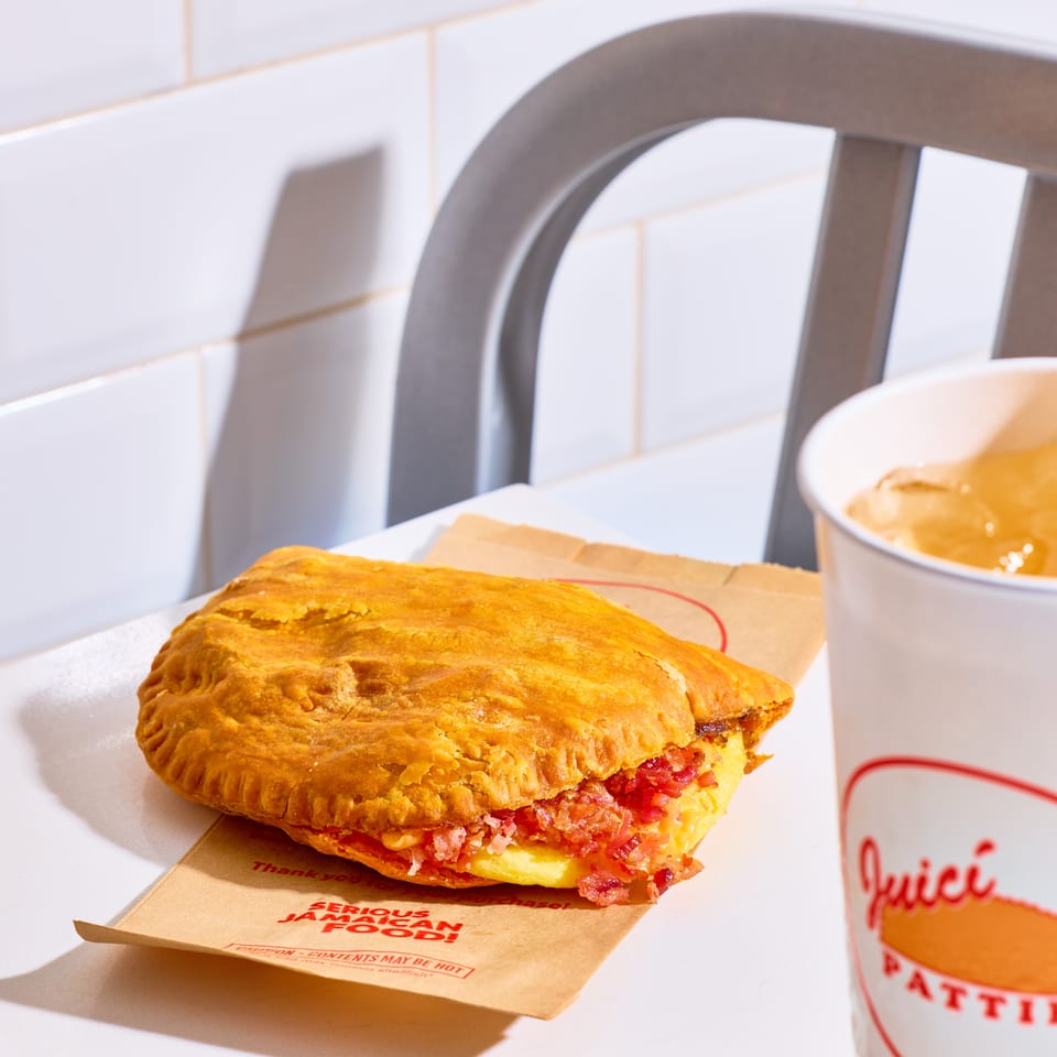 Golden flaky pastry sandwich with bacon and egg beside a branded cup on a white café table.