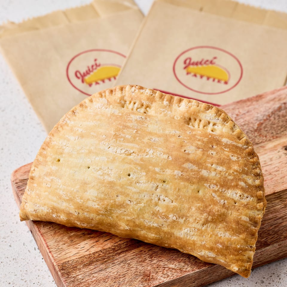 Golden, flaky baked pastries rest on a wooden cutting board beside branded paper bags.