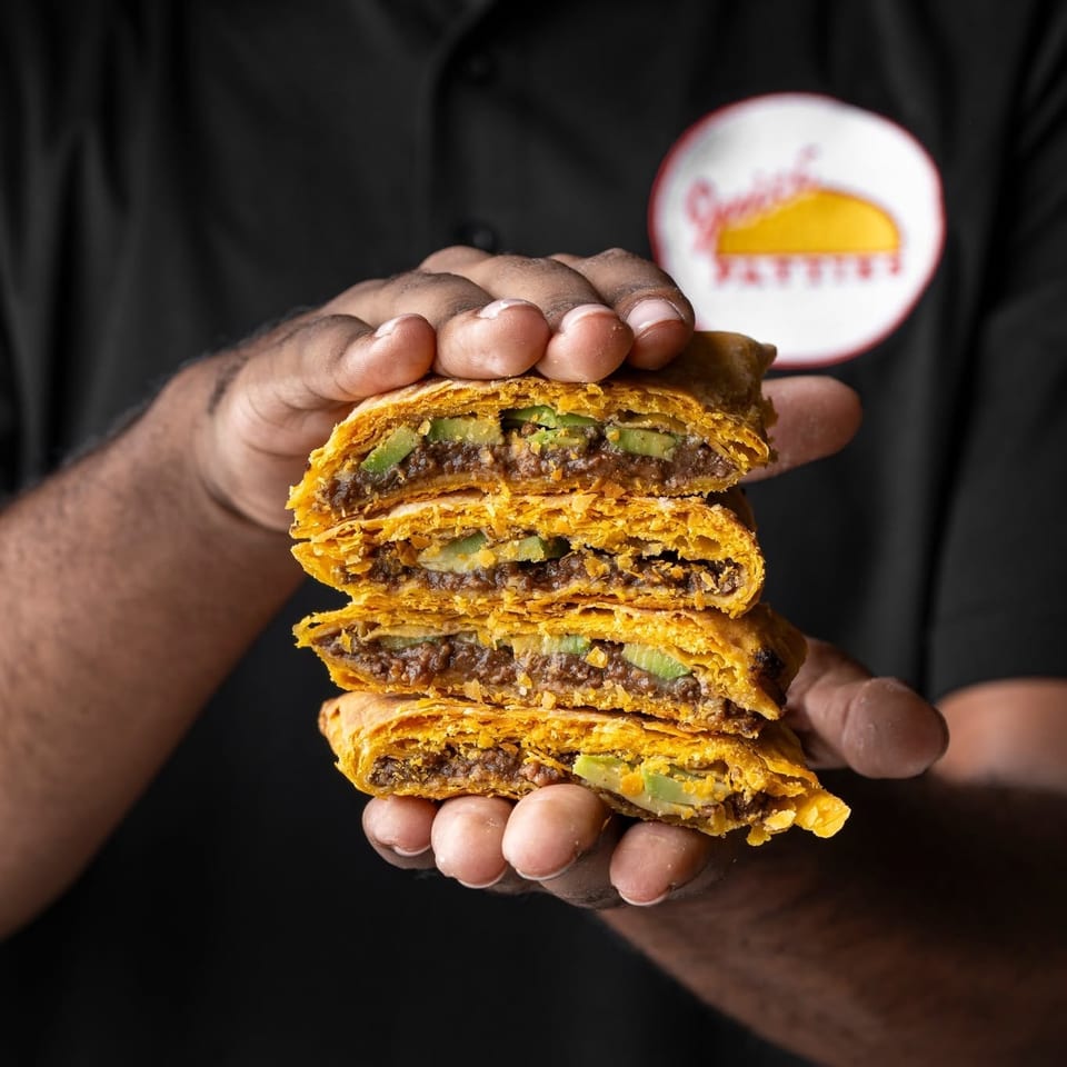 Person in black shirt holds stacked, flaky pastry burgers filled with beef patties, melted cheese, and pickles.