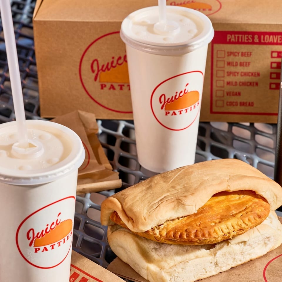 Juicy Patties sandwich with flaky pastry filling, two fountain drinks, and branded takeout boxes in a shopping cart.
