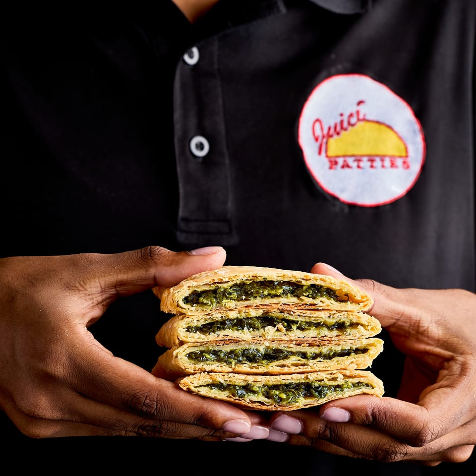 A chef in a black uniform holds stacked flaky pastries filled with seasoned greens.