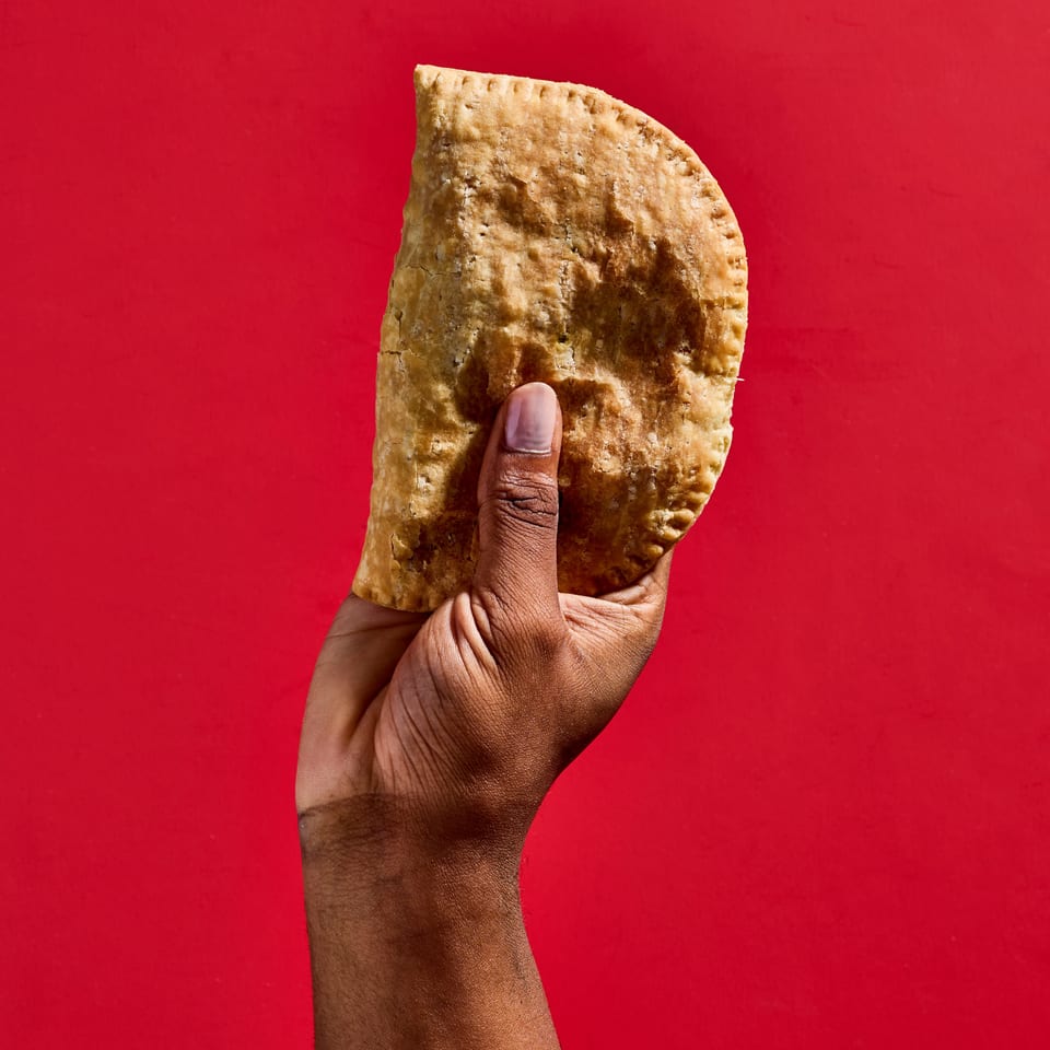 Hand holding a golden-brown, folded grilled flatbread against a vivid red background.