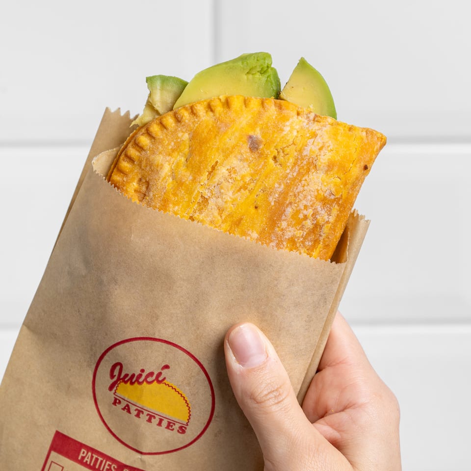 Golden pastry filled with avocado is held in a branded paper sleeve.